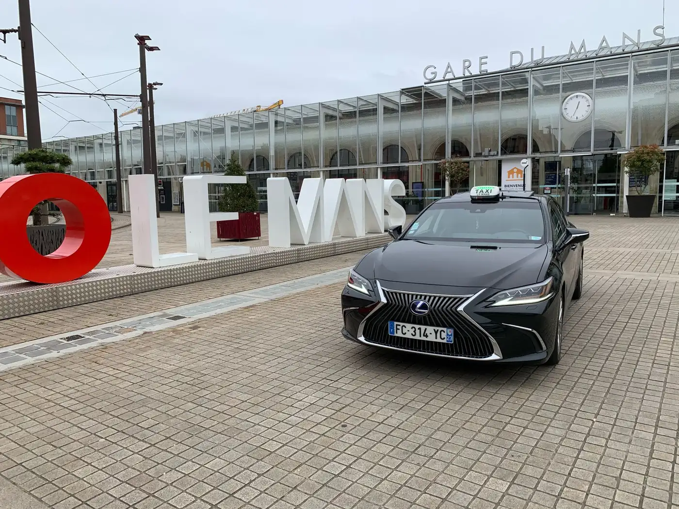 La berline noire de Taxi Bouti, enseigne taxi sur le toit, garée devant les lettres LE MANS et la gare du Mans